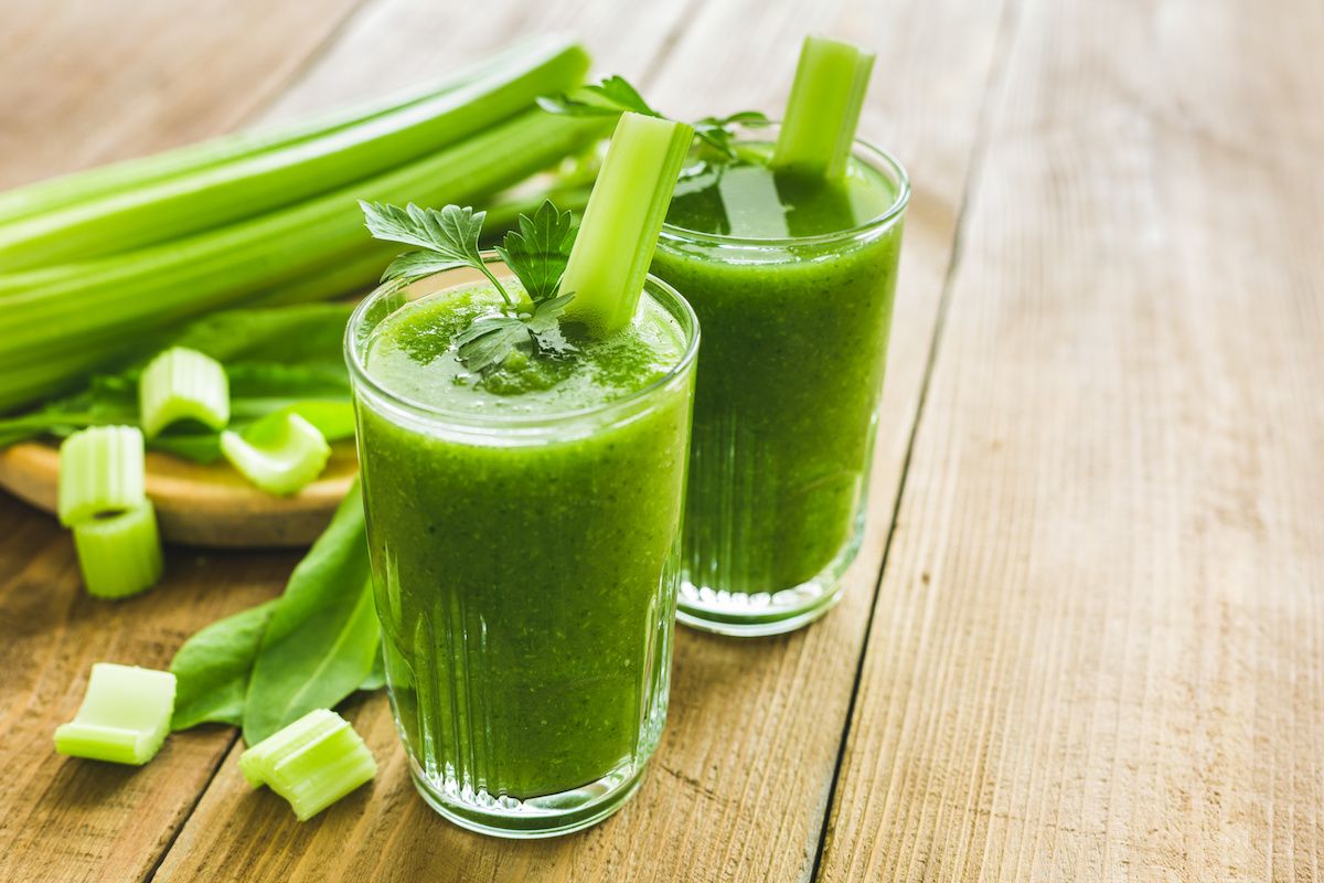 Two cups of celery juice on a table with chopped celery behind them