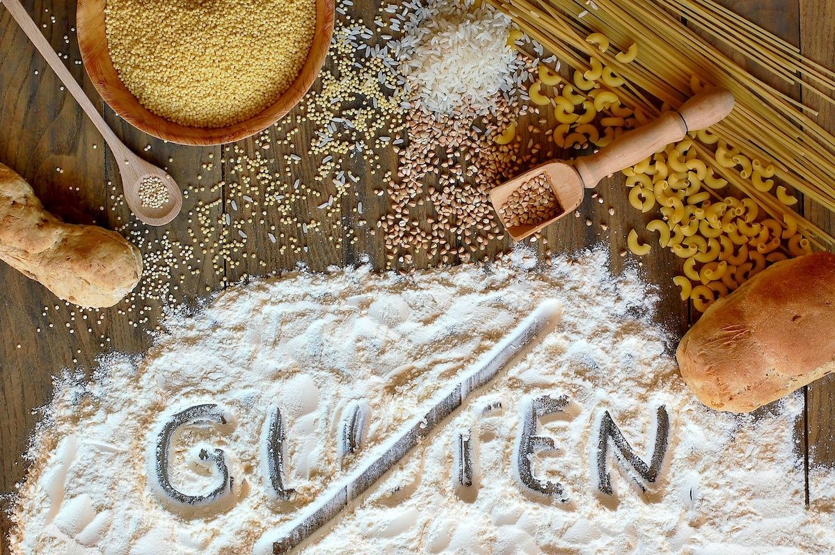 Various grains and pastas arranged arround the word "gluten" that is crossed out