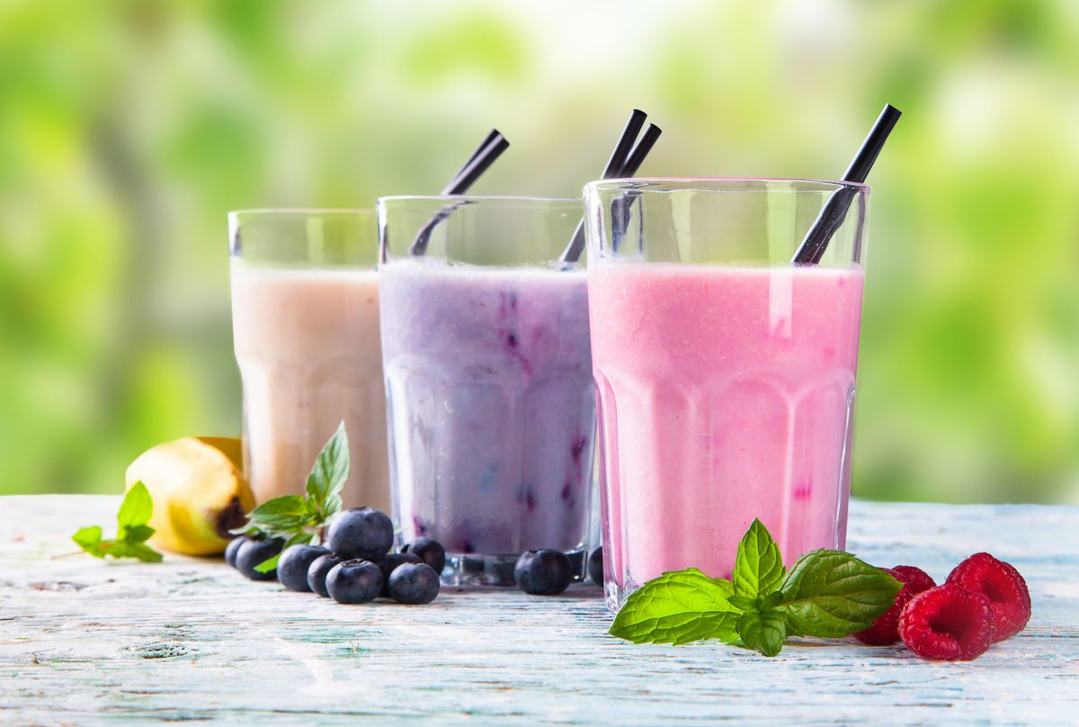 Three smoothies on a table surrounded by fruit