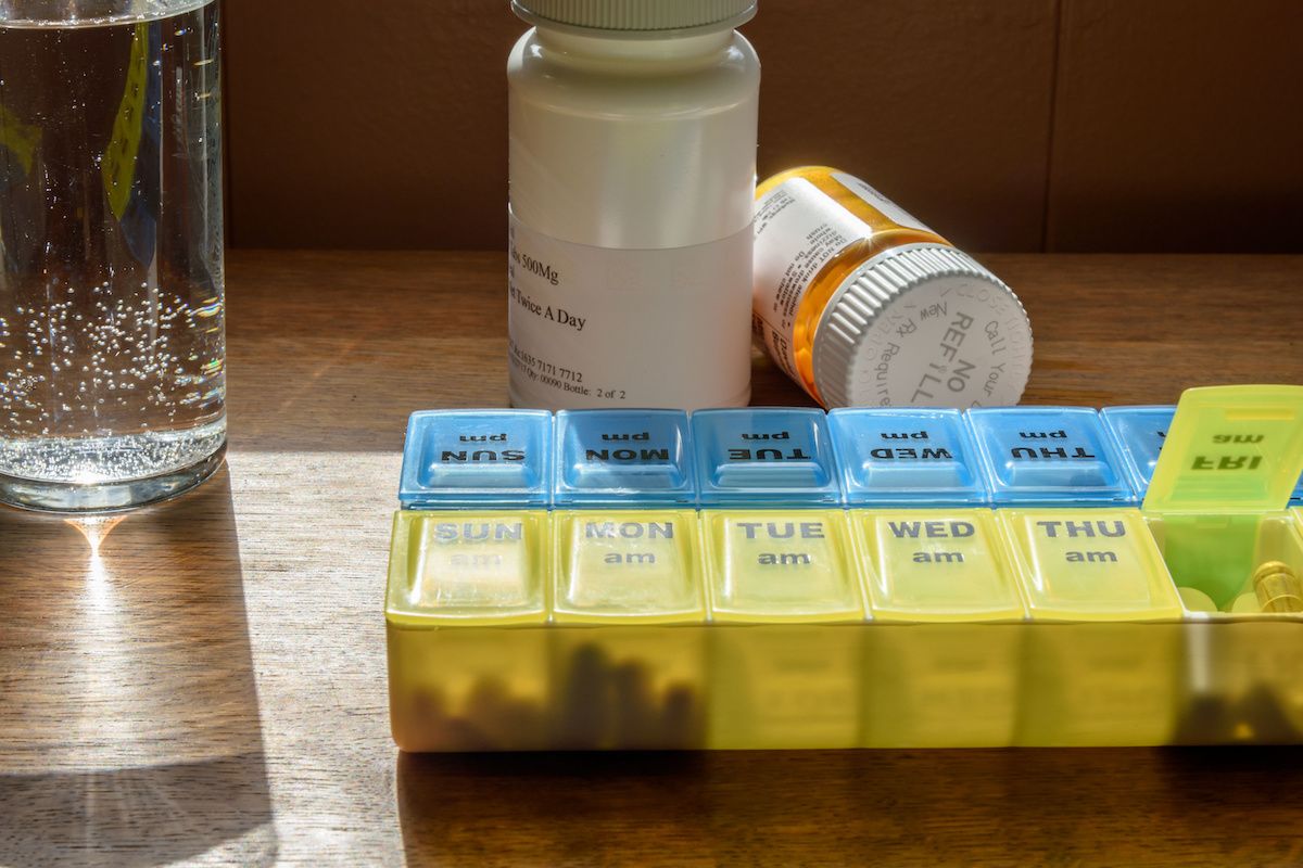 A pill dispenser box with a glass of water and medication bottles