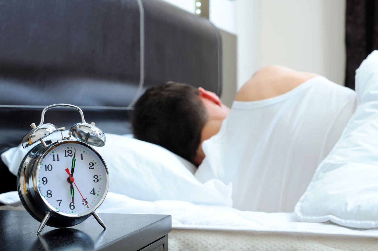 Person sleeping in bed with alarm clock on bedside table