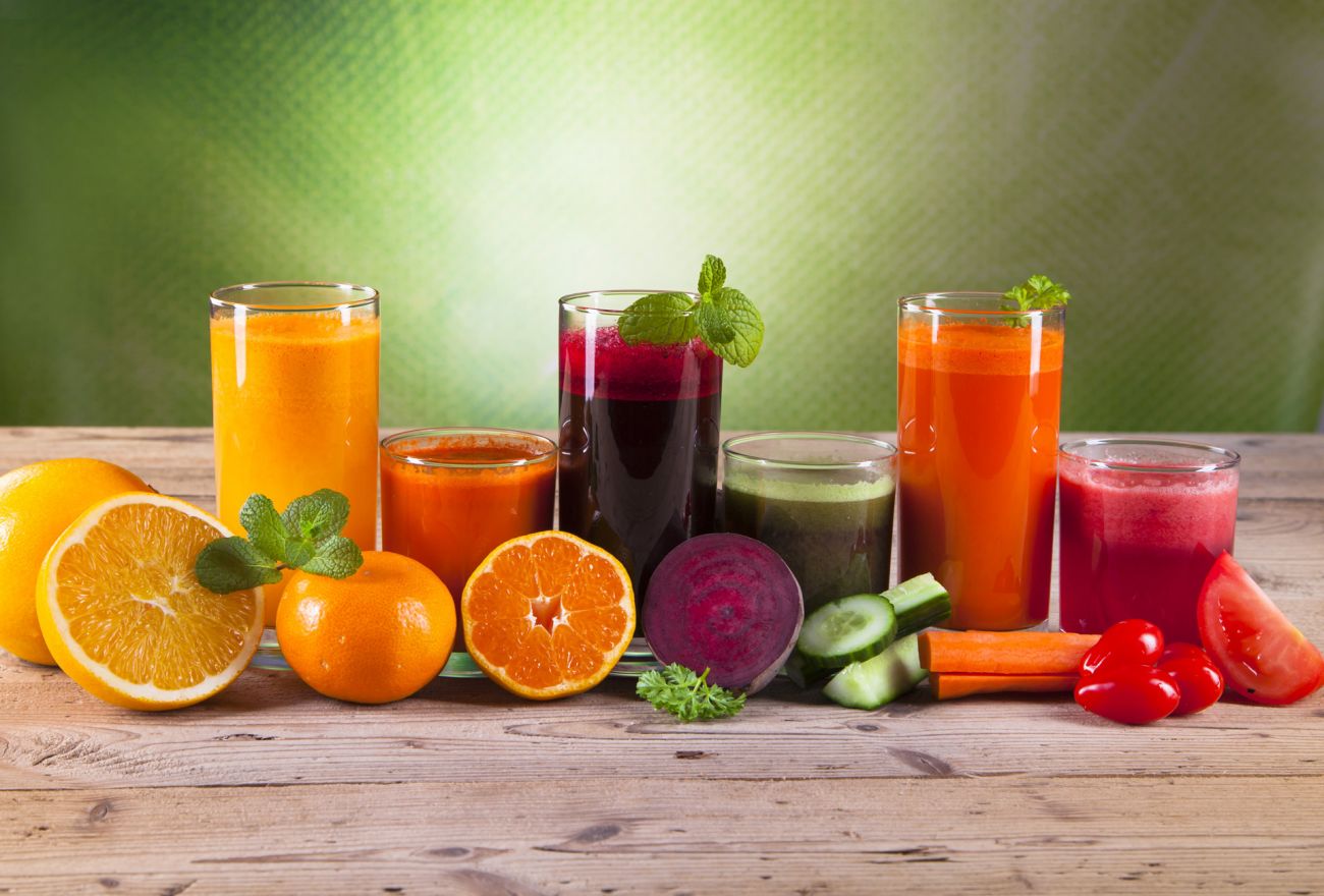 Healthy fruits and vegetables in front of cups of fruit and vegetable juice