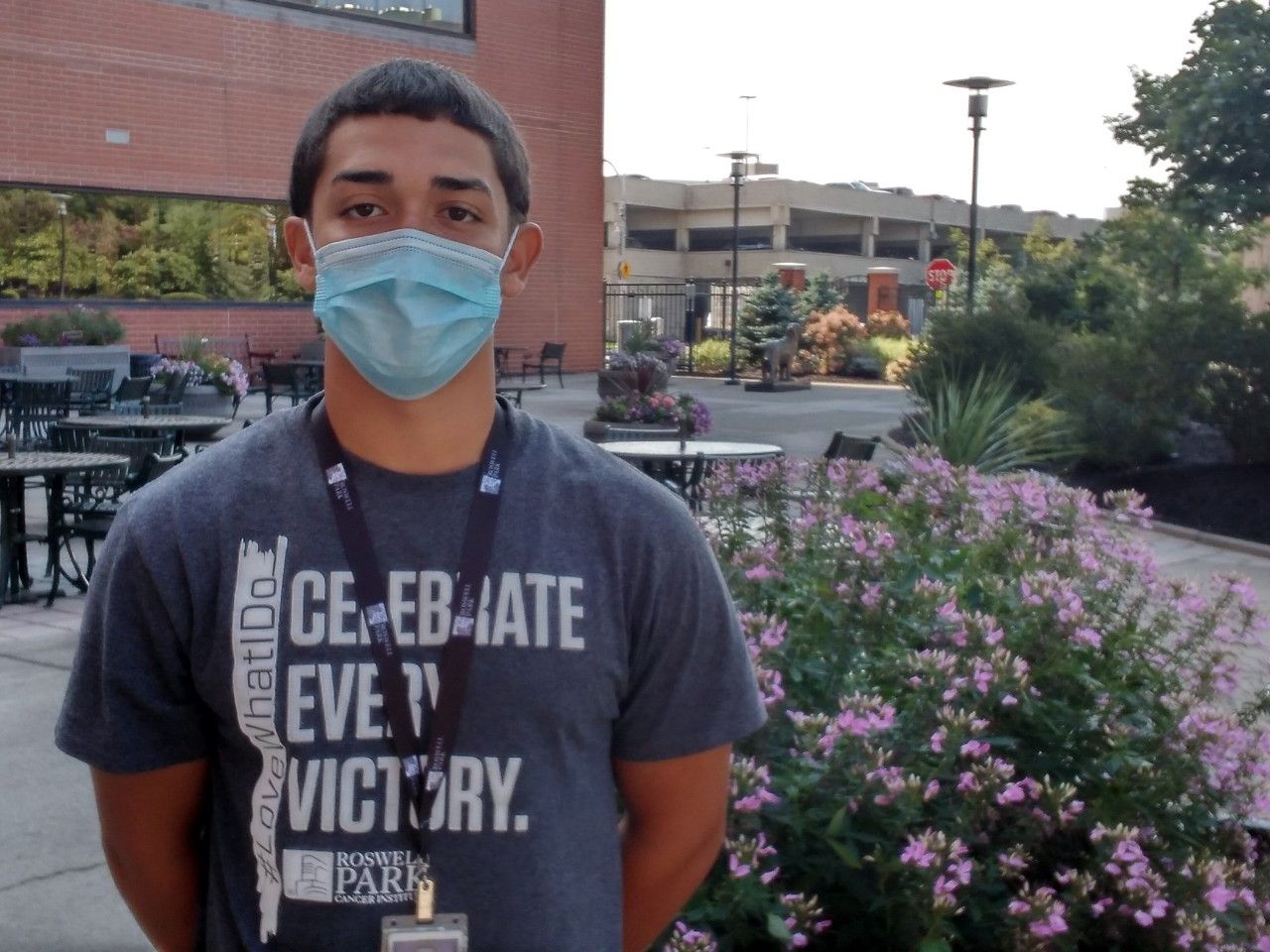 Young man wearing a face mask stands in front of flowers inside Kaminski Park.