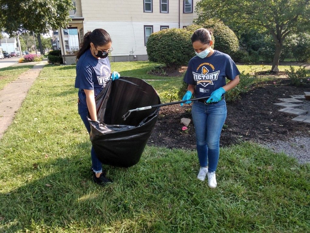 One young woman holds a large plastic garbage bag as another deposits trash while they work to clean up the Fruit Belt neighborhood. 