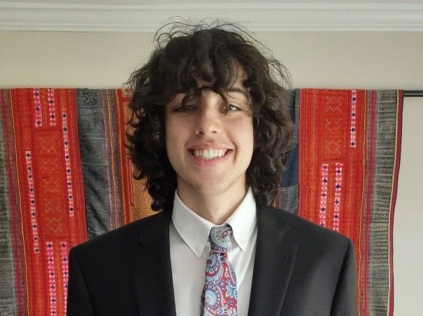 Young man with curly hair smiles while standing in front of a striped curtain.