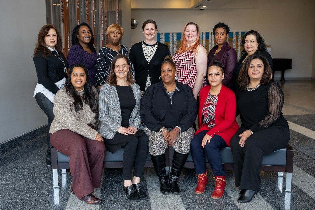 A group of 12 women, representing the Office of Community Outreach and Education at Roswell Park, gather in a lobby.  