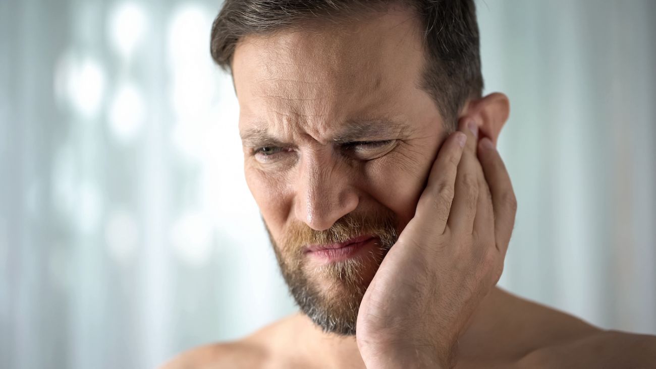 Man holds his ear and grimaces in pain - stock