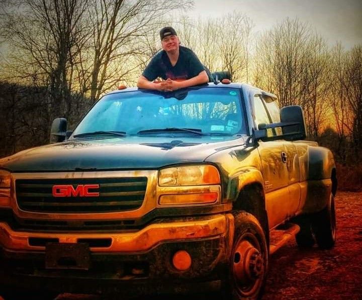 A young man lays across the top of a muddy pickup truck.