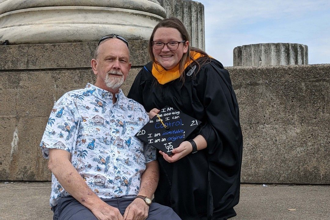 Jerry and Haley Ward sit on concrete steps as she holds up her cap after graduating from college. 