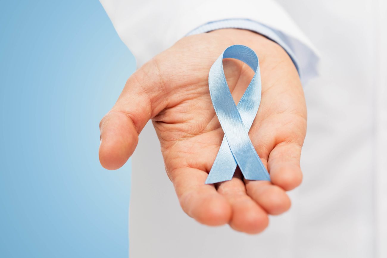 A person in a lab coat holds a blue ribbon in their hand, the awareness ribbon for prostate cancer. 