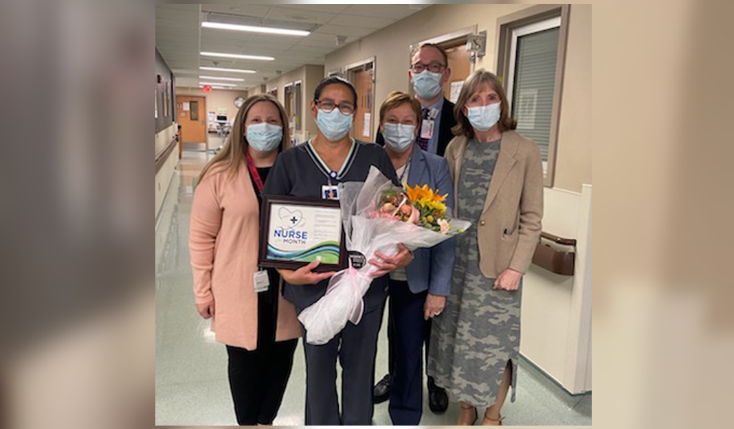 Cindy Latimore, second from left, holds a bouquet of flowers and a certificate, given to her for being named Nurse of the Month for May. She is standing in a hallway with other members of the Roswell Park staff, including President and CEO Candace S. Johnson. 