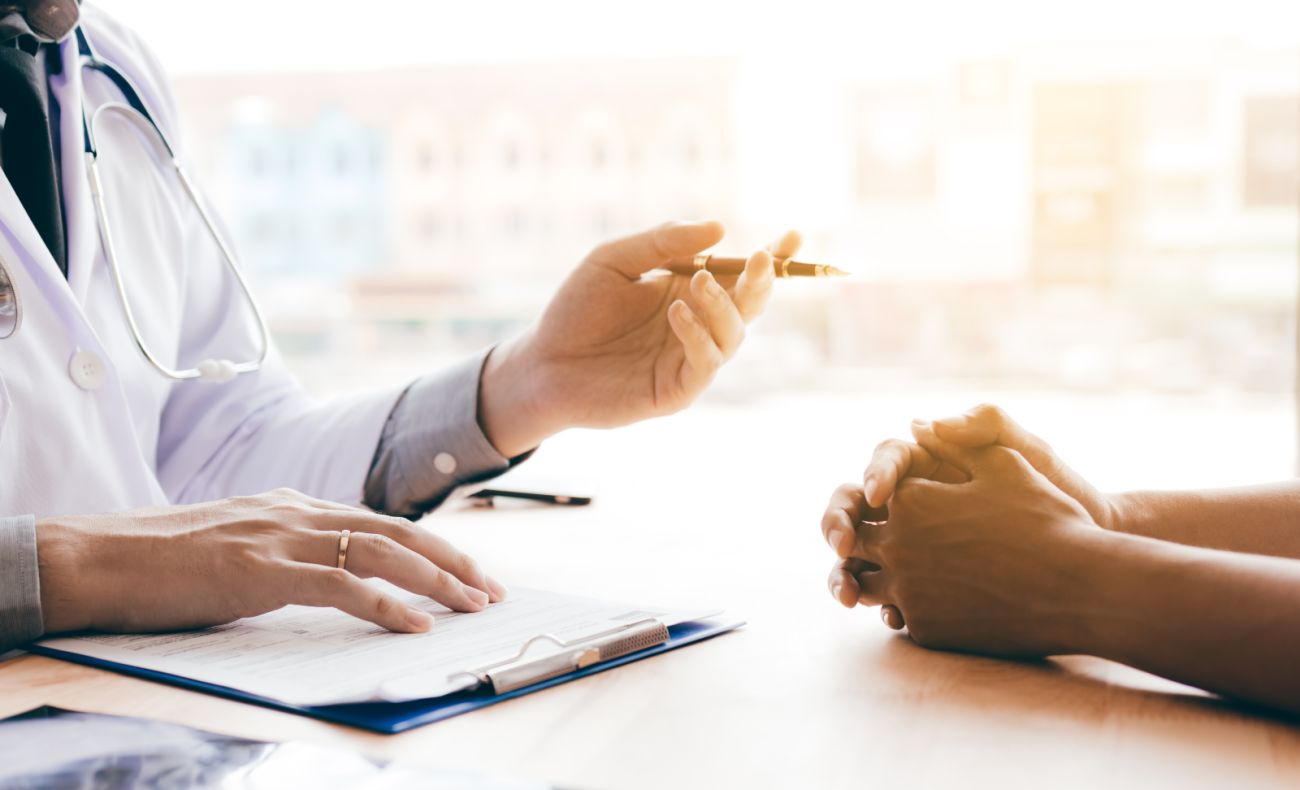 person in white coat gestures to person with clasped hands