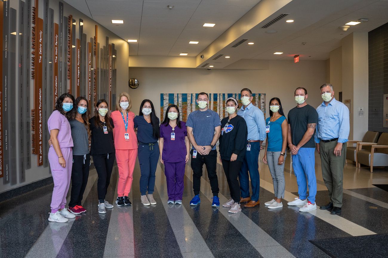 A group of physical therapists stands together, wearing masks, in a lobby. 
