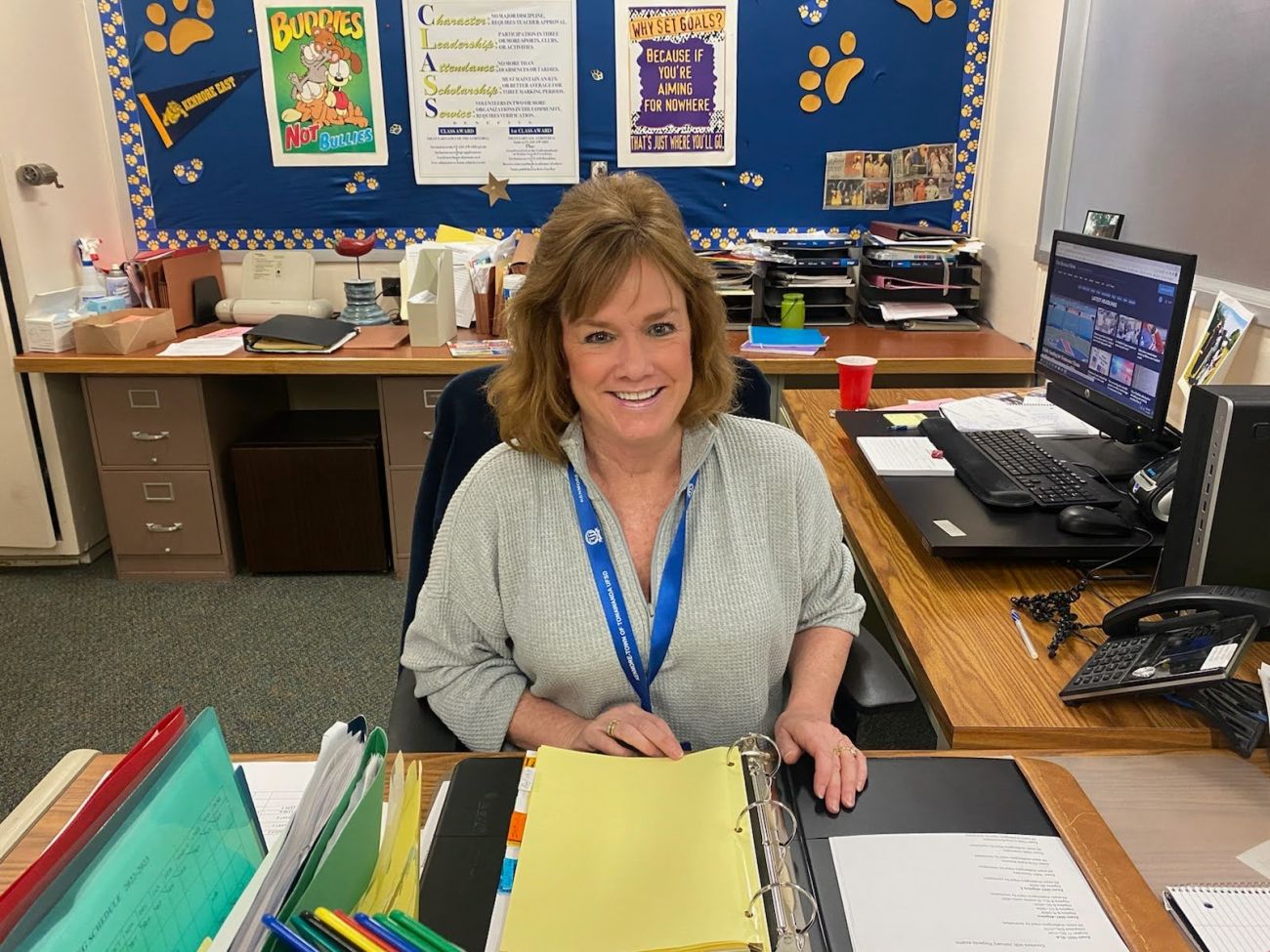 A woman sits at a desk in a school office. 