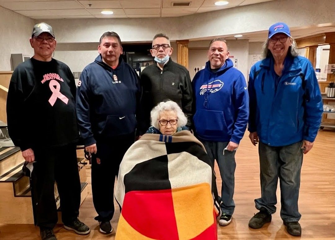 Carolyn Henry sits in a wheelchair, covered by a blanked with red, black, white and yellow segments, in front of her sons (L-R) Dale, Rob (Bear), Ron (Mouse), Brian and Ray. 