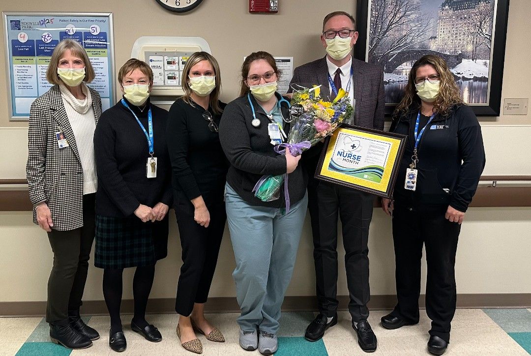 Delaney Finewood, center, holds a bouquet of flowers for being named Nurse of the Month. She is in a hallway with three other women and one man. 