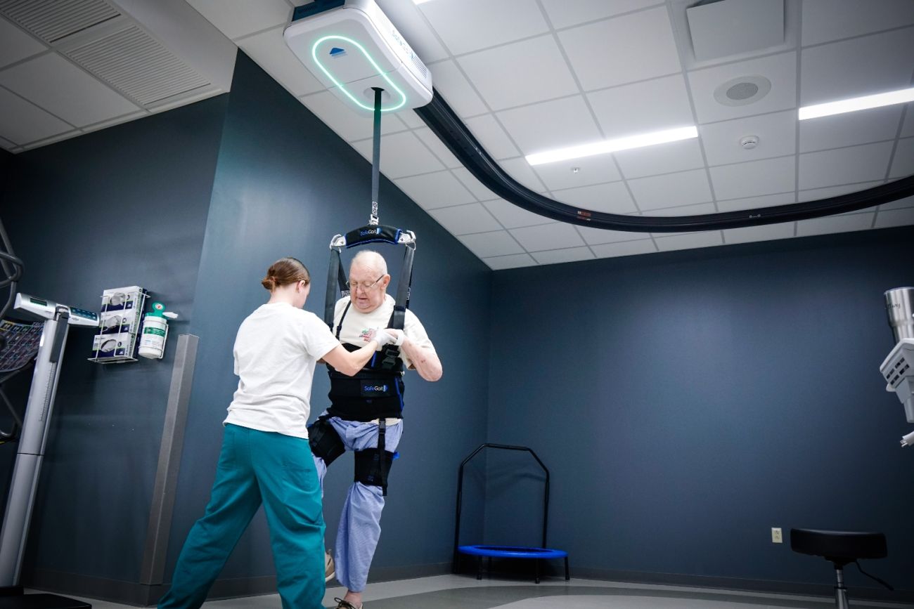 a physical therapists helps a man strapped into a harness