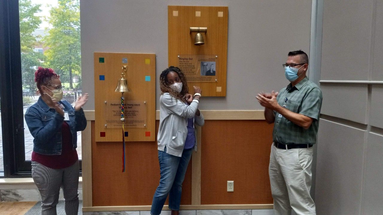 A woman in a purple hoodie rings the Victory Bell after completing a long surveillance period for cervical cancer and mesothelioma. 