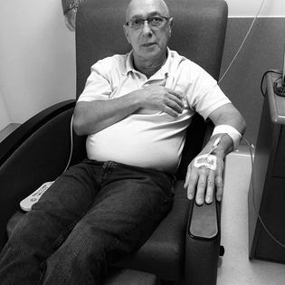 A black and white photo of a man sitting in a chemotherapy infusion chair receiving treatment. 