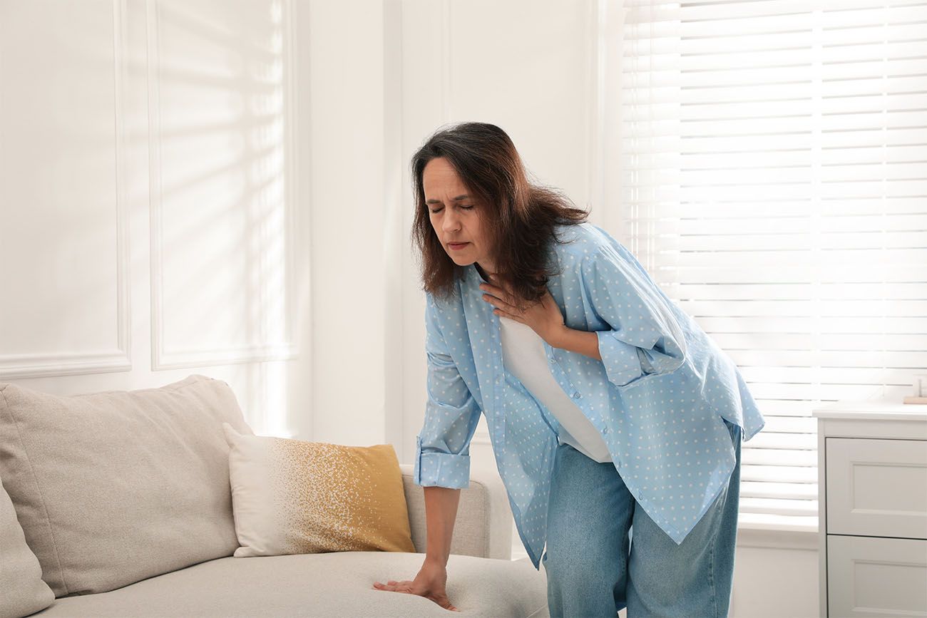 older woman holding her chest with one hand steading herself on the couch with the other