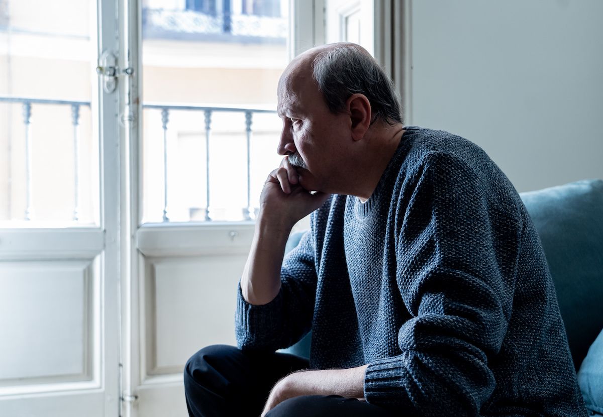 Older man looks solemnly out of a window