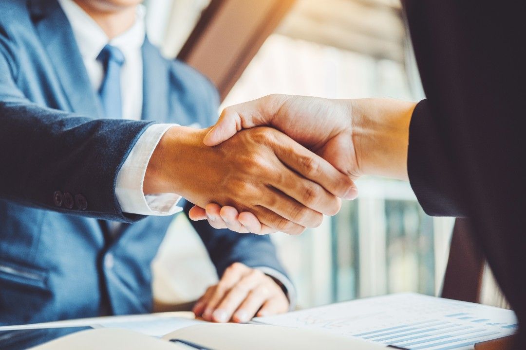 stock image of two people shaking hands over paperwork. 