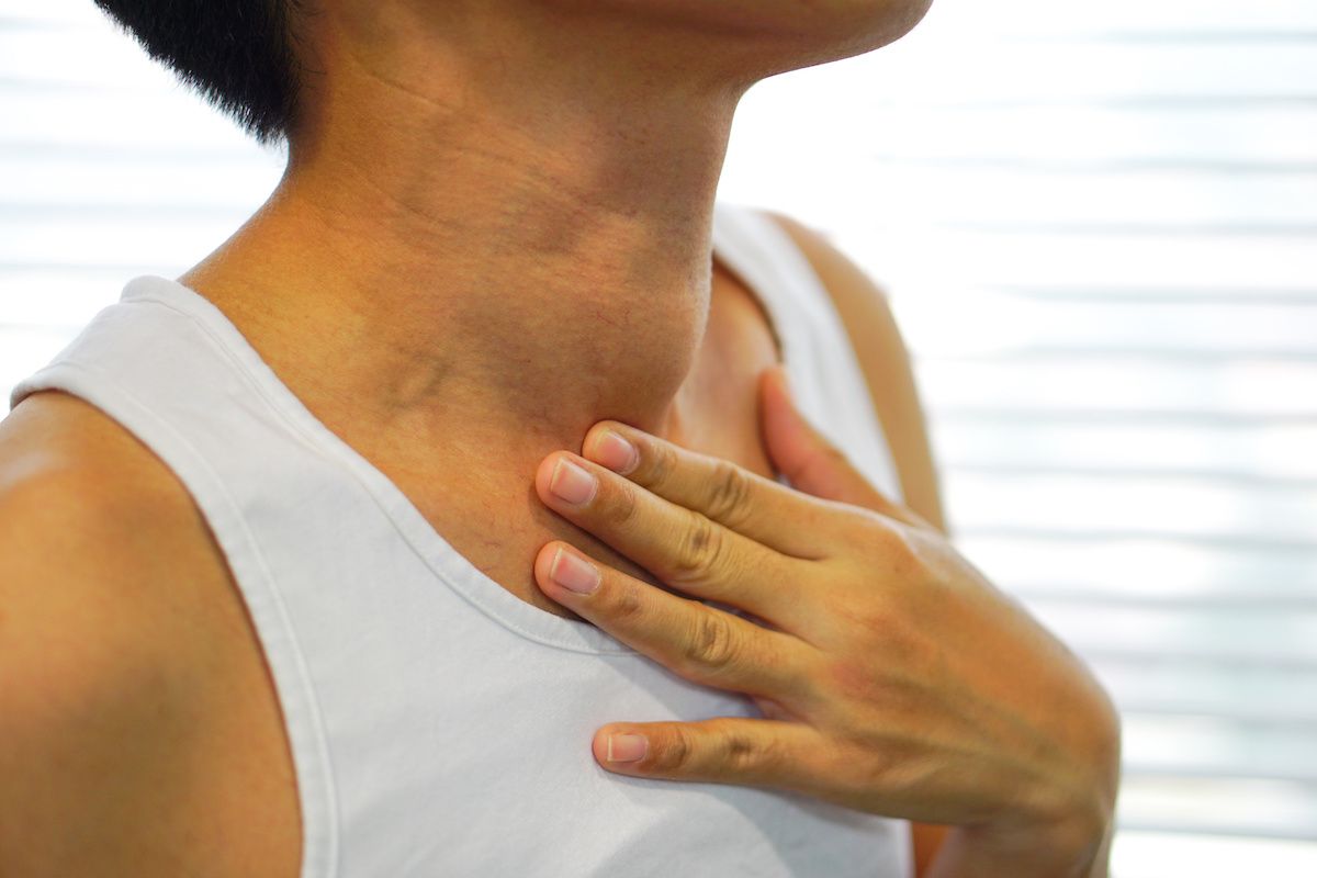 Woman tipping her head and touching her neck near her thyroid