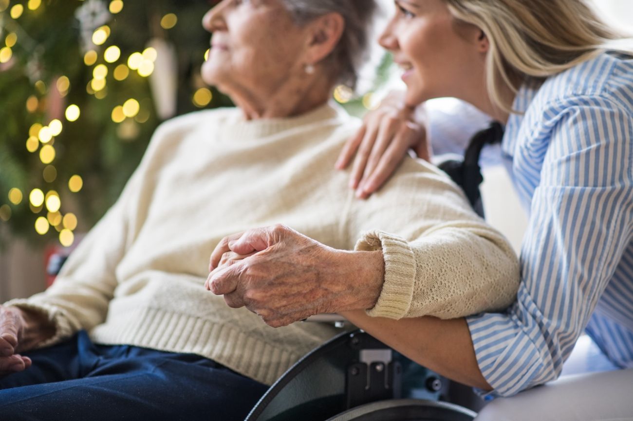 Young woman holds on older woman's hand in a wheelchair, while looking at a Christmas tree