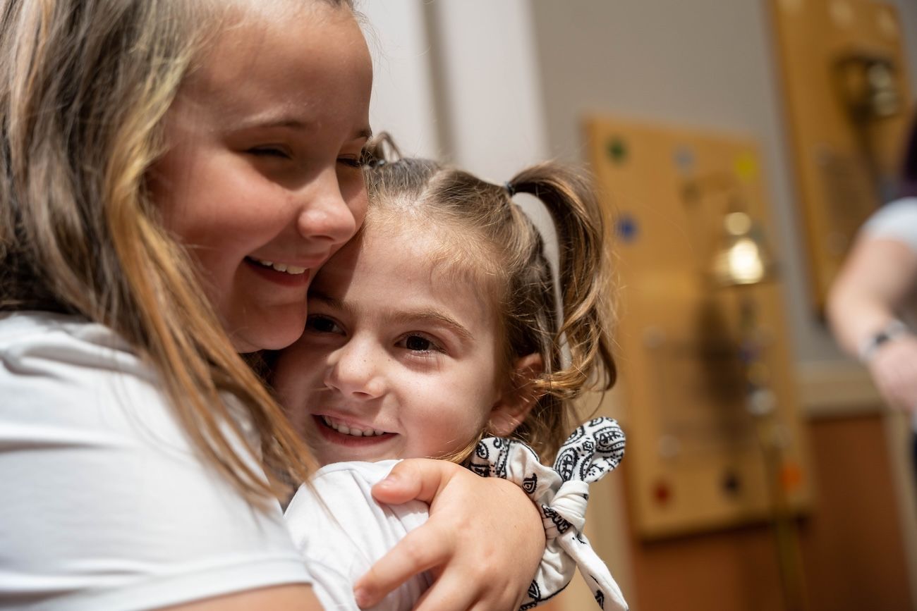 Pediatric patient Lily hugs a friend in the lobby at her Victory Bell Ringing