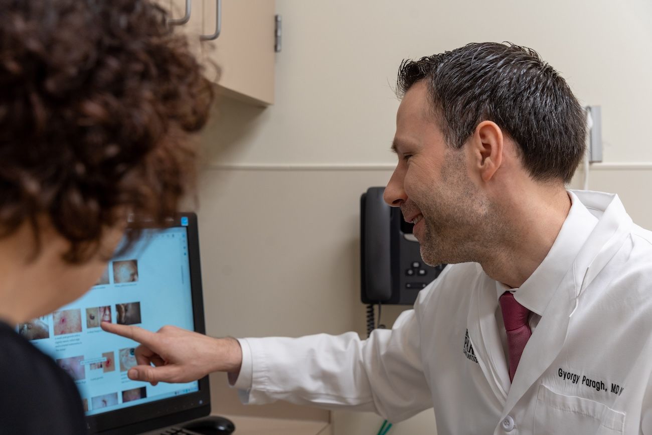 Dr. Gyorgy Paragh looks at a computer screen in clinic with a patient