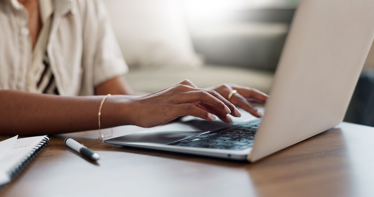 Close up of a person's hands typing onto a computer while sitting at a desk.