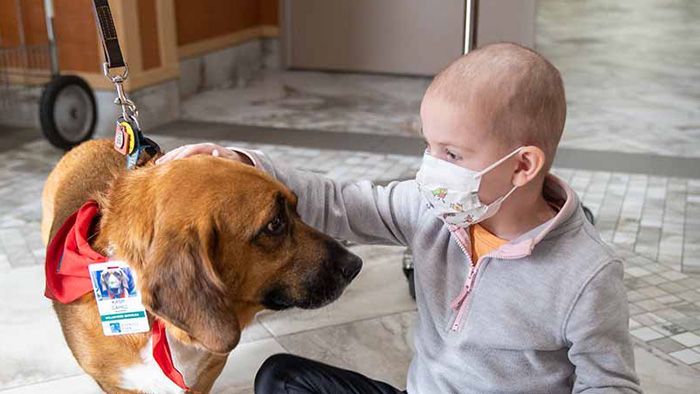 A young girl sits on the floor of a clinic petting a therapy dog. 