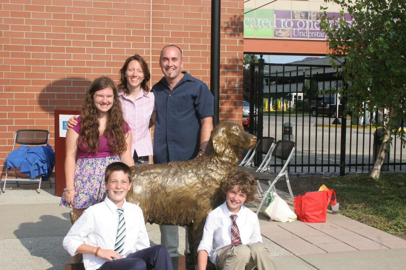 Nicole Gerber stands with her family alongside a statue of Monty, Roswell Park's first therapy dog