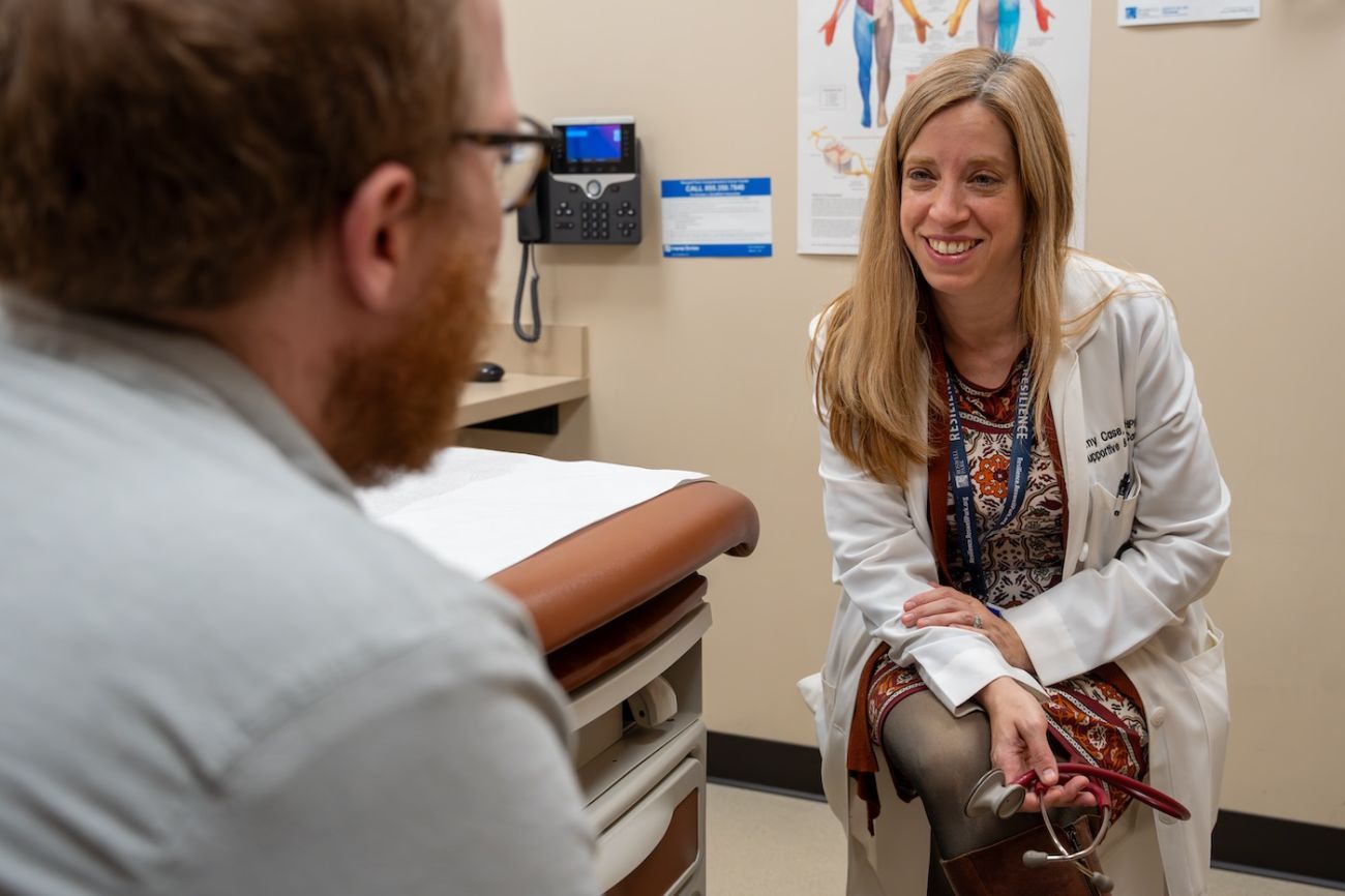 Dr. Amy Case, Chair of Supportive and Palliative Care, sits in clinic with a male patient