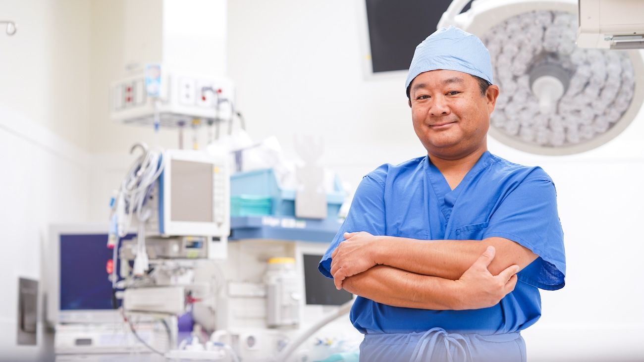 Dr. Kazuaki Takabe poses in scrubs and his arms cross in the surgical suite 