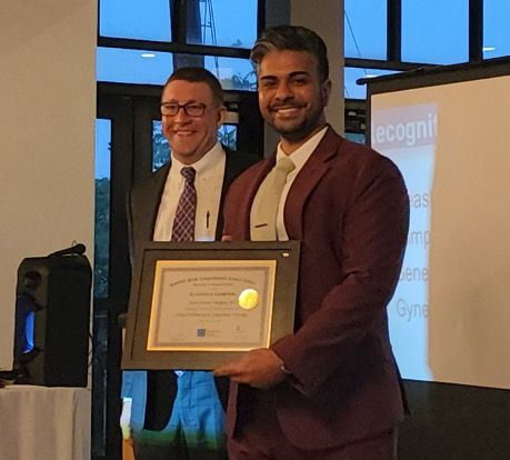 Dr. Peter Frederick stands with GYN fellow Aaron Varghese holding an award