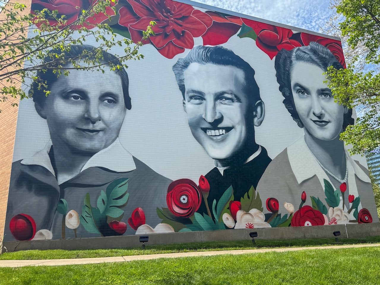 An outdor mural shows three faces in black and white framed in red and green flowers