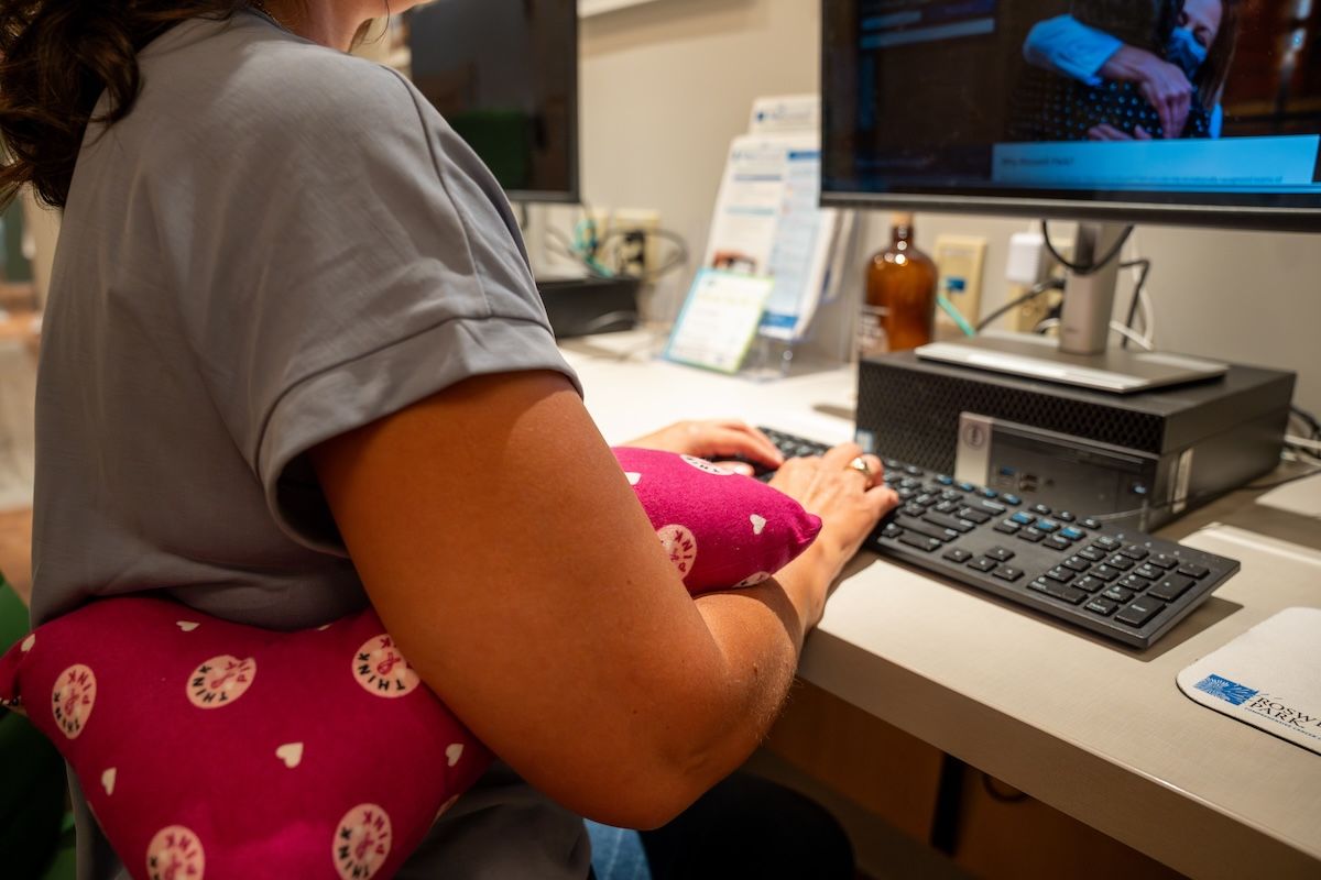 Photo of woman demonstrating use of mastectomy pillow placed under arm.