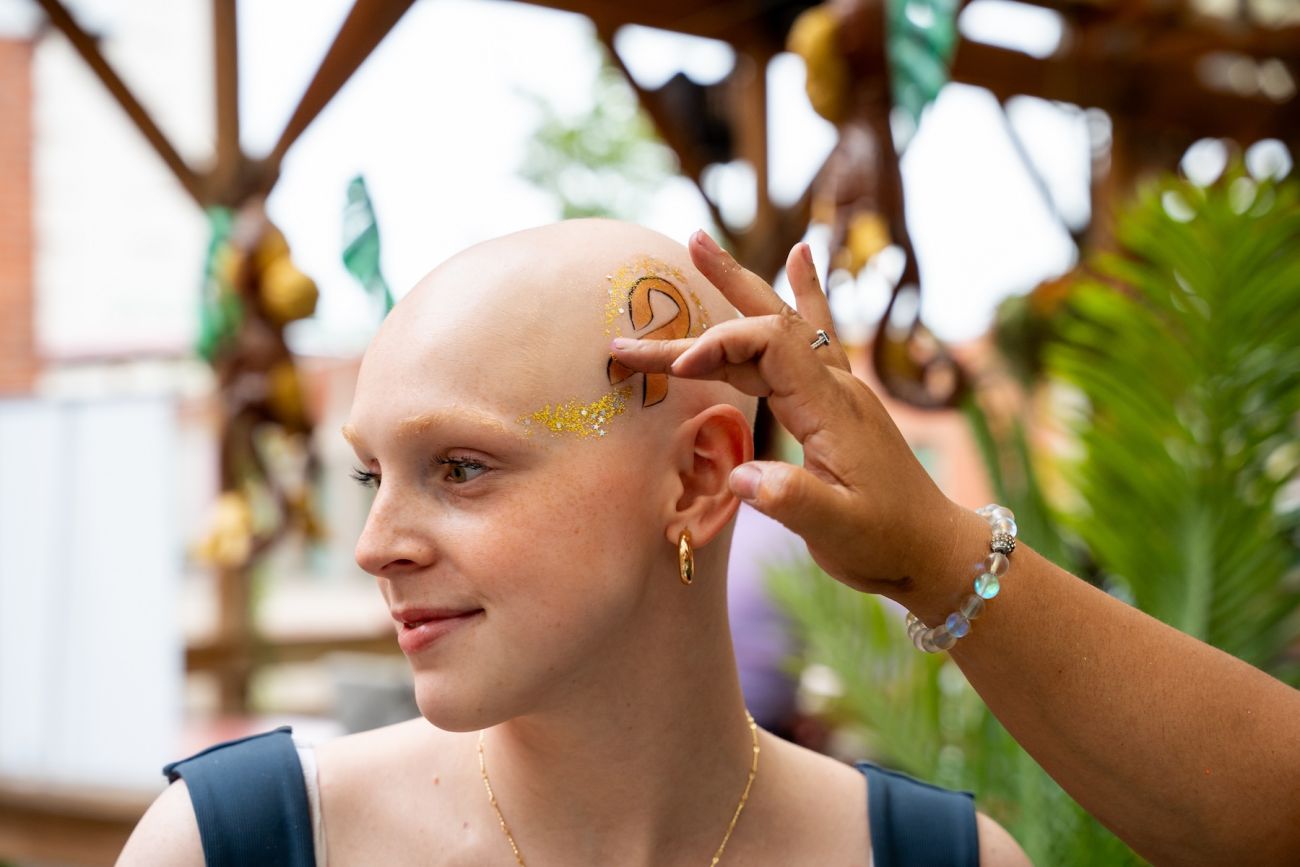 A cancer survivor gets a cancer ribbon painted on the side of their head