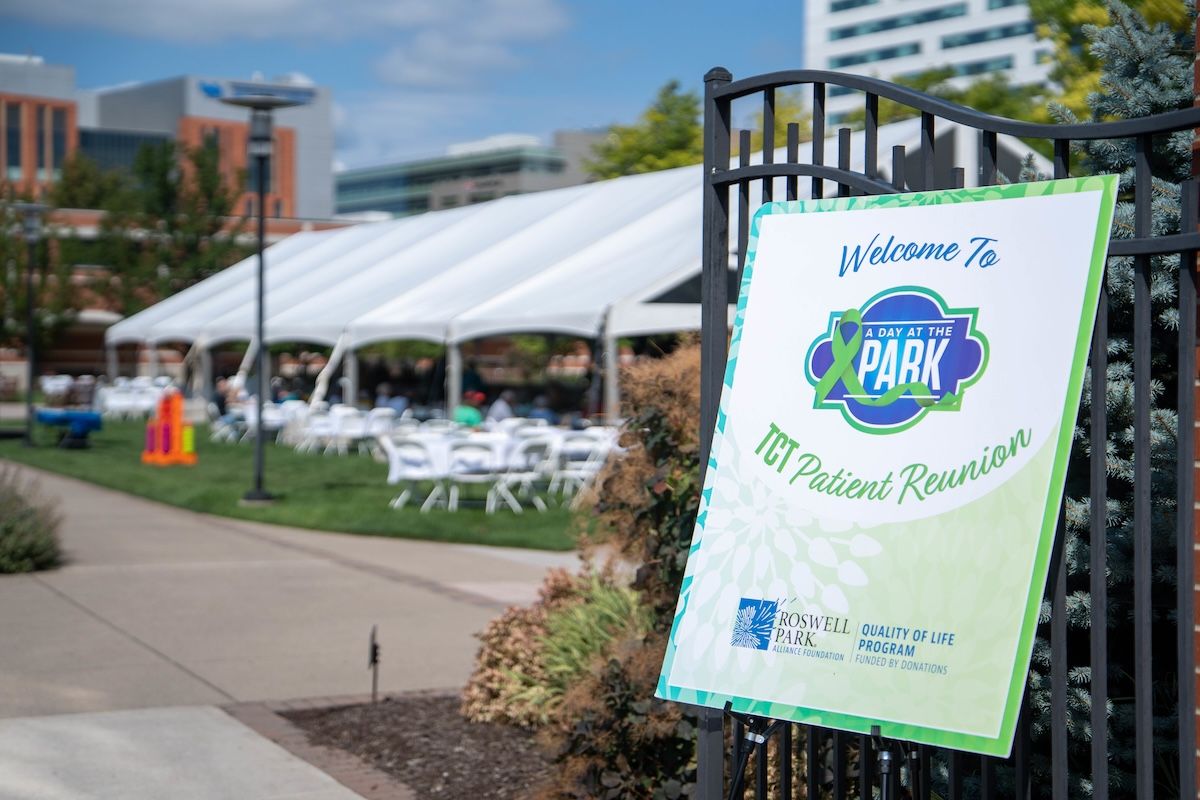 A sign for an outdoor event in a park under a tent