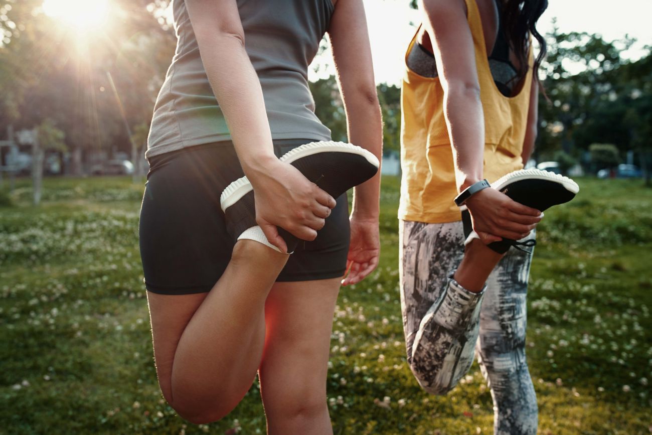 Close shot of two women on the grass, stretching their legs before a walk or run