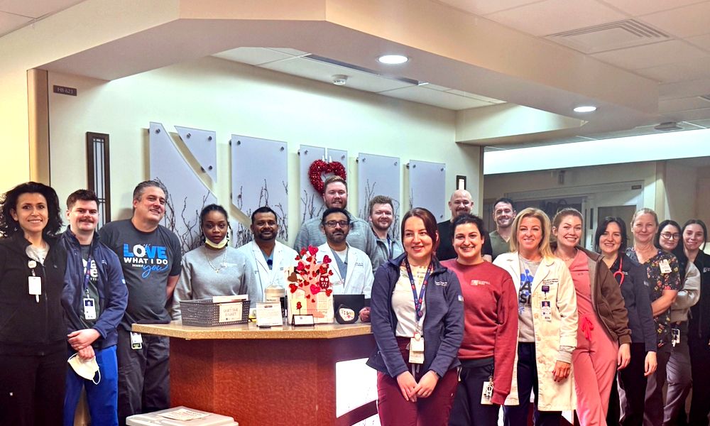 A group of about 20 clinical workers pose for a photo around an inpatient hospital unit