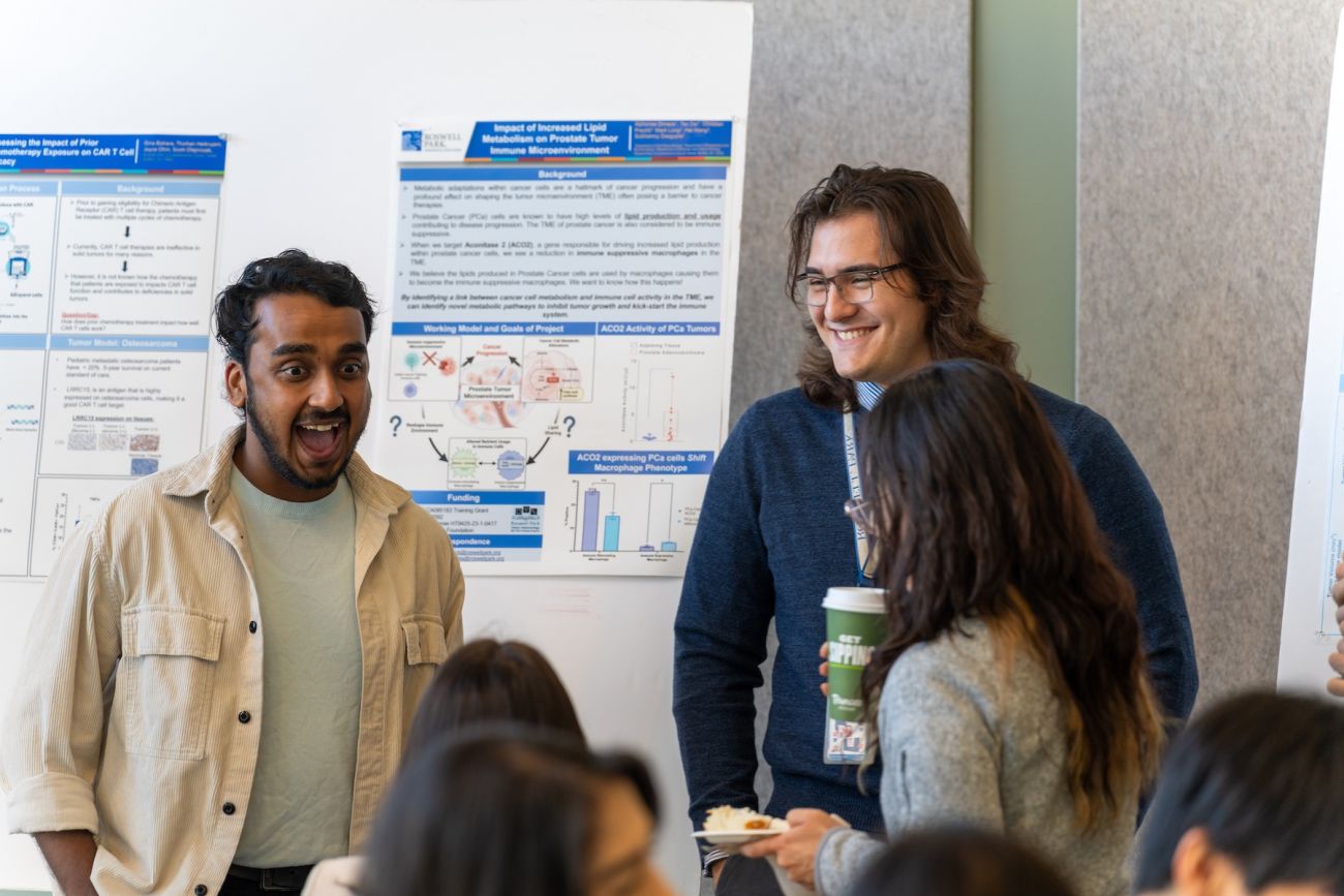 Two students laughing in front of a research poster at an event