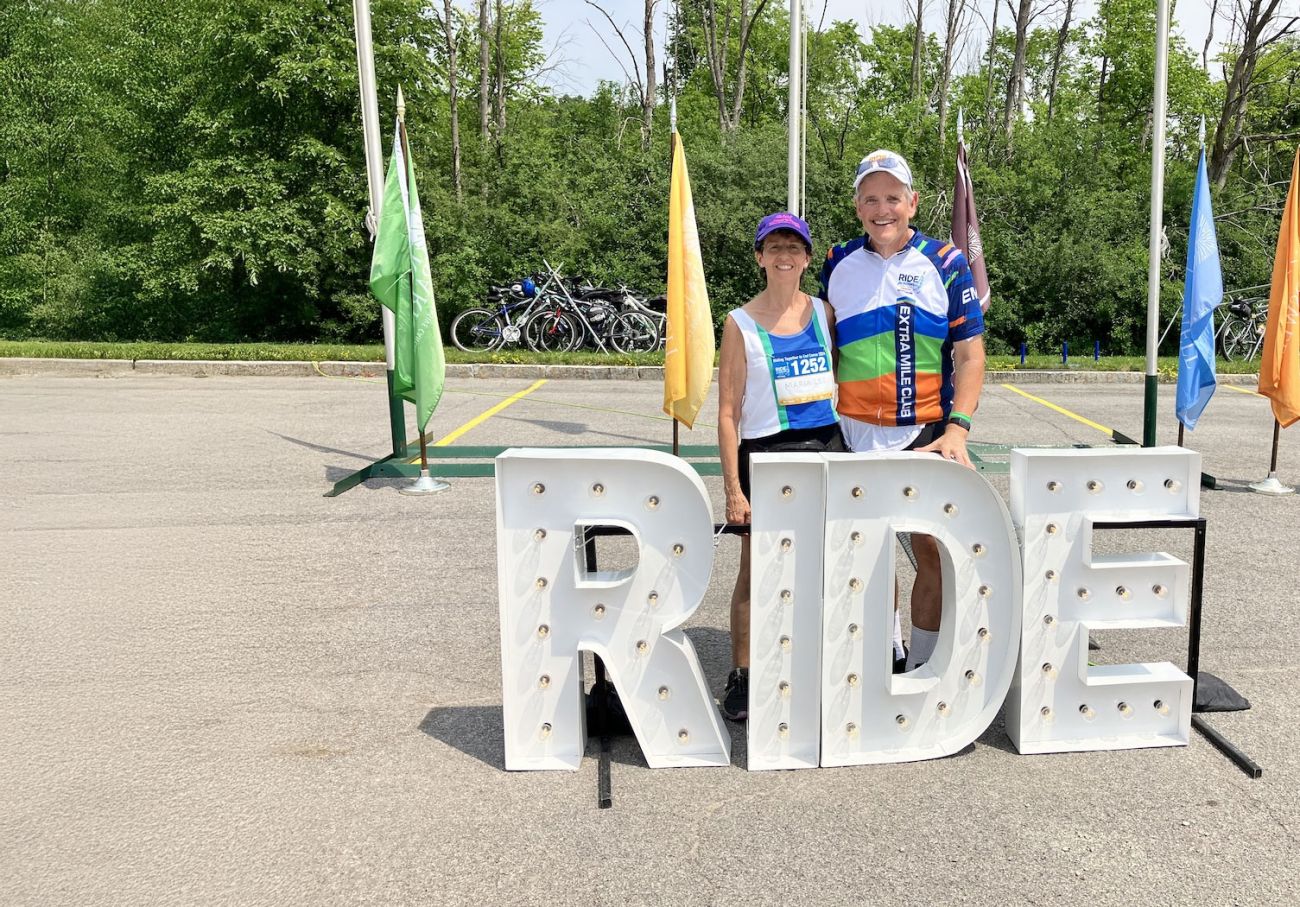 A couple pose with a large sign for Ride for Roswell