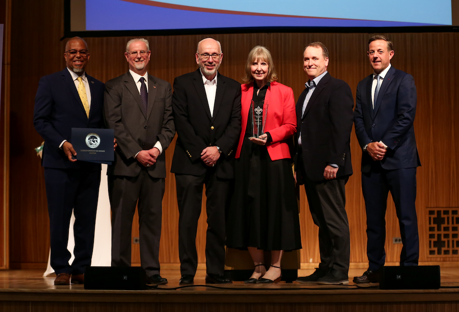 Woman in red jacket receives award next to five men