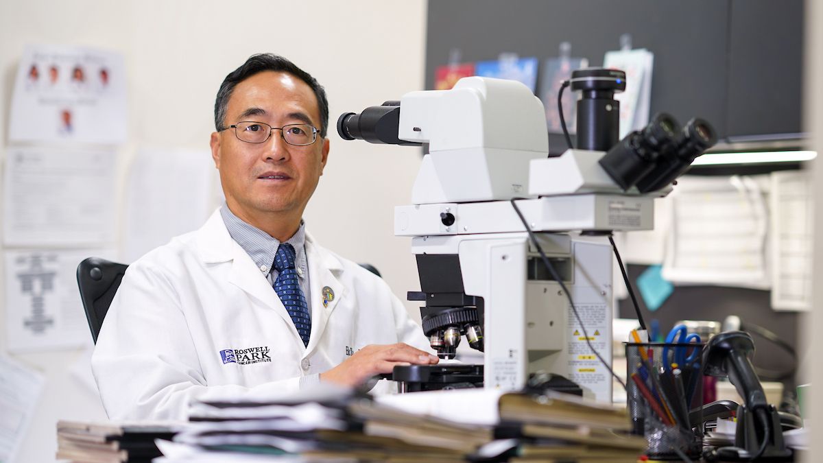 Dr. Bo Xu sits at a microscope in a lab