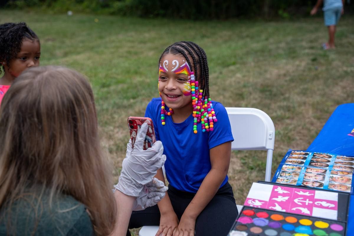 A young child smiles at their reflection after seeing their face painted in bright colors.