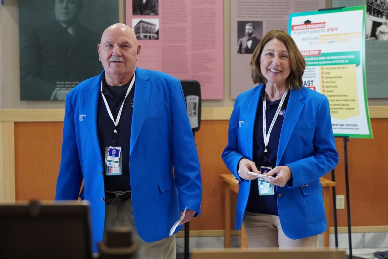 Two volunteers in bright blue blazers look to help patients in a hospital