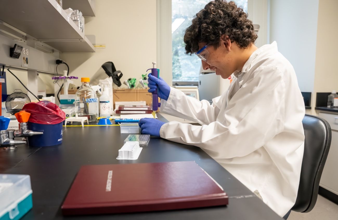 A male high school intern in the SURE-CAN Program works at a lab table 