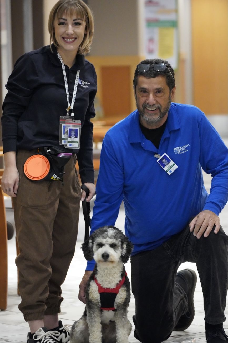 A volunteer escorts a therapy dog and their owner around a hospital